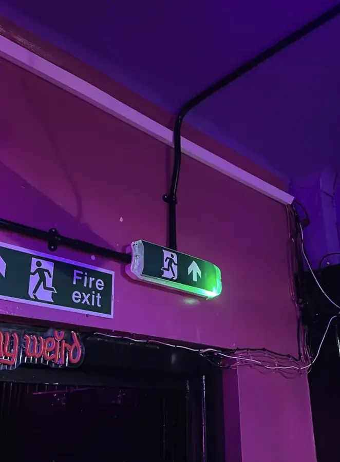 An illuminated fire exit sign and emergency light fitted in a Lincoln bar
