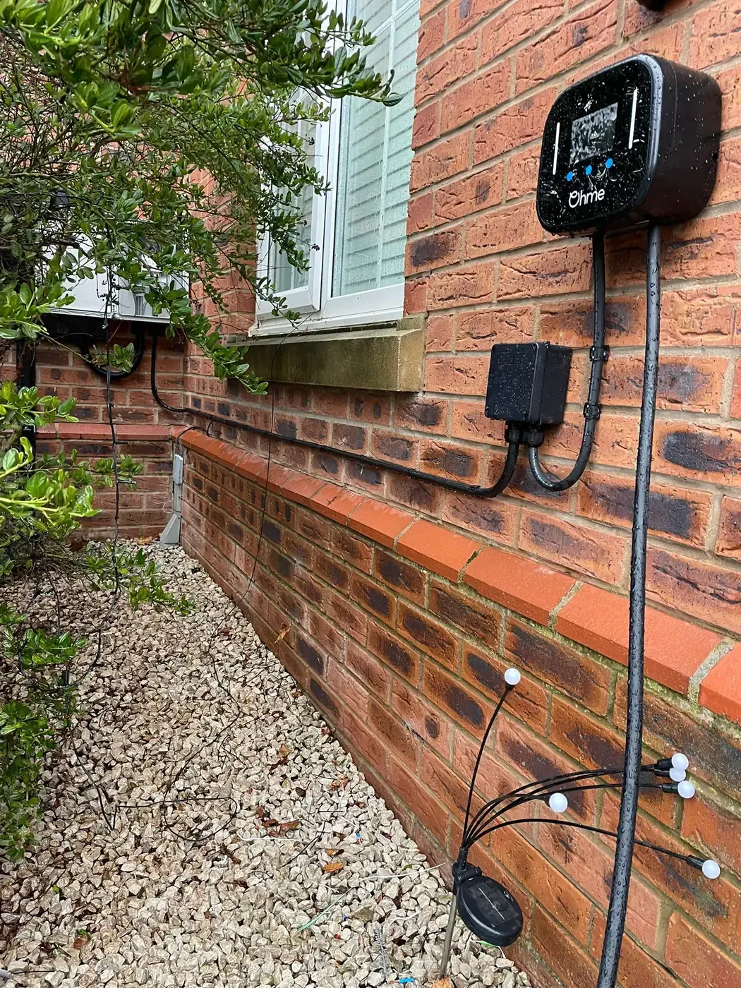 A home EV charger fitted to a red brick wall in a Lincoln garden
