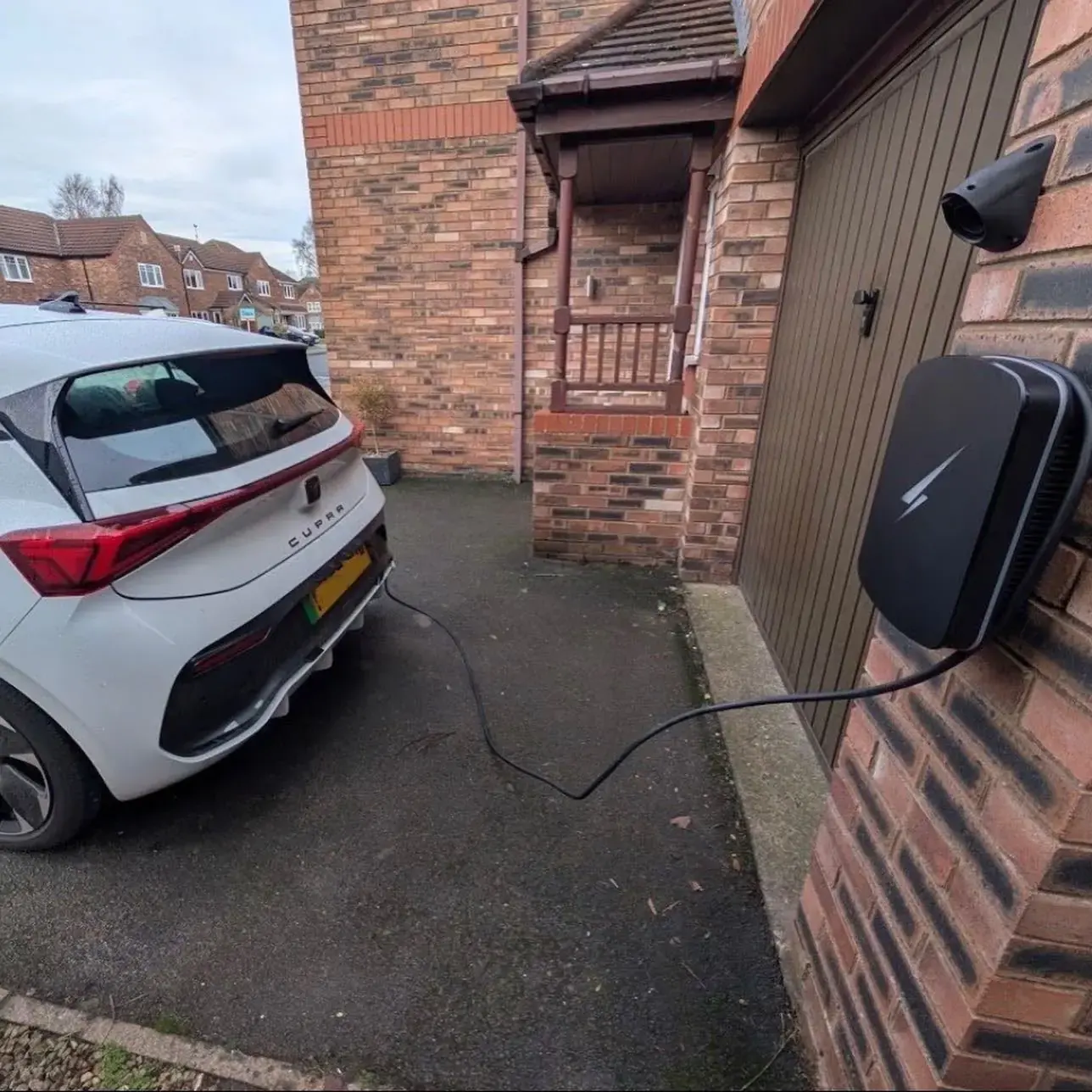 An electric car charging from a home charger on a driveway